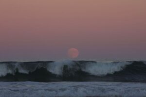 Pełnia księżyca nad ciemnymi falami oceanu o zachodzie słońca