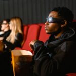 Widzowie w okularach 3D siedzą w kinie z pudełkami popcornu.