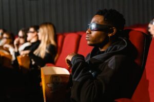 Widzowie w okularach 3D siedzą w kinie z pudełkami popcornu.