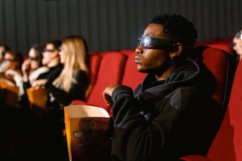 Widzowie w okularach 3D siedzą w kinie z pudełkami popcornu.