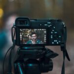 Aparat Sony na statywie z wyświetlaczem pokazującym nagrywany obraz mężczyzny w okularach.