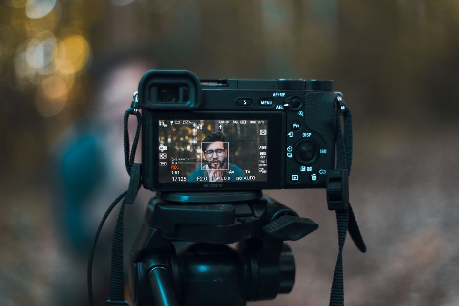 Aparat Sony na statywie z wyświetlaczem pokazującym nagrywany obraz mężczyzny w okularach.