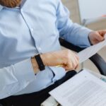 Mężczyzna w błękitnej koszuli czyta dokumenty trzymając w dłoni złoty długopis