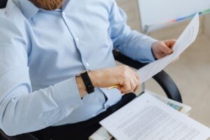 Mężczyzna w błękitnej koszuli czyta dokumenty trzymając w dłoni złoty długopis
