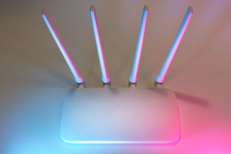 Biały router z czterema antenami oświetlony niebieskim i różowym światłem