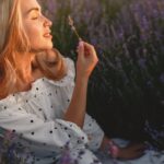 Kobieta w białej sukience wąchająca gałązkę lawendy na polu w słońcu