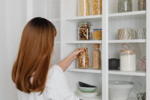 Kobieta układająca szklane słoiki z produktami spożywczymi na białej półce kuchennej