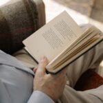 Mężczyzna w jasnej koszuli czyta otwartą książkę z tekstem poetyckim.