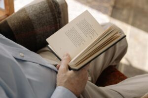 Mężczyzna w jasnej koszuli czyta otwartą książkę z tekstem poetyckim.