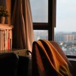 Fotel z kocem przy regale z książkami obok okna z widokiem
