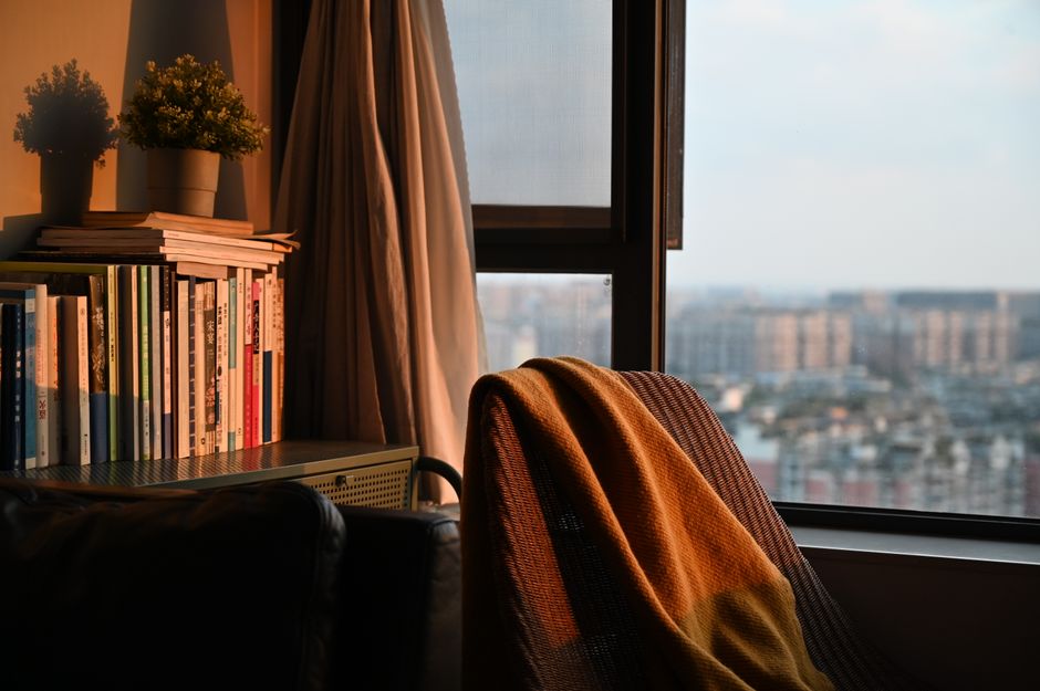 Fotel z kocem przy regale z książkami obok okna z widokiem
