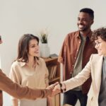 Mężczyzna i kobieta witają się uściskiem dłoni w obecności dwojga współpracowników
