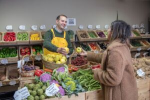 Sprzedawca w żółtym fartuchu podaje jabłko klientce w sklepie warzywnym