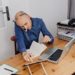 Mężczyzna przy biurku rozmawia przez telefon, korzystając jednocześnie z laptopa i tabletu.