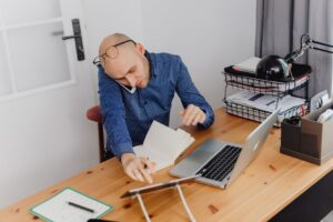 Mężczyzna przy biurku rozmawia przez telefon, korzystając jednocześnie z laptopa i tabletu.