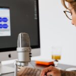 Osoba w słuchawkach nagrywa podcast przed mikrofonem i monitorem z falą dźwiękową