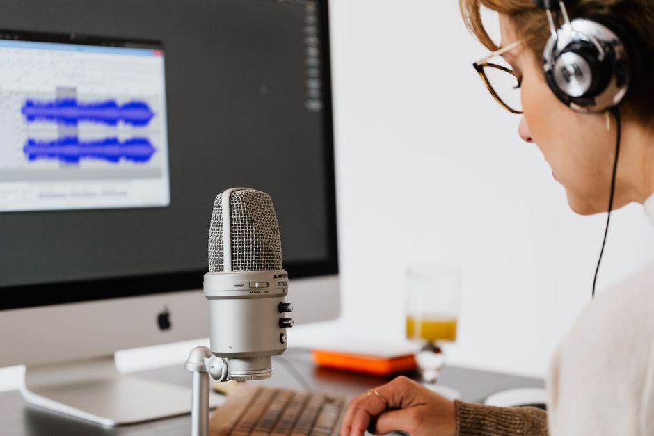 Osoba w słuchawkach nagrywa podcast przed mikrofonem i monitorem z falą dźwiękową