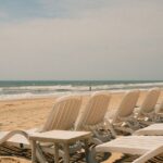 Puste białe leżaki ustawione w rzędzie na piaszczystej plaży przy morzu