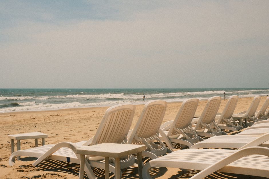 Puste białe leżaki ustawione w rzędzie na piaszczystej plaży przy morzu
