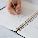 Dłoń zapisująca ołówkiem plan dnia w otwartym notesie spiralnym