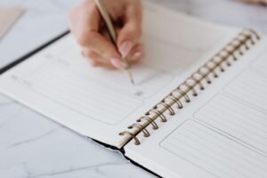 Dłoń zapisująca ołówkiem plan dnia w otwartym notesie spiralnym