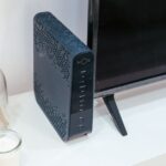 Czarny router NOS stojący na białej szafce obok telewizora