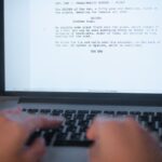 Dłonie piszące scenariusz filmowy na klawiaturze laptopa.
