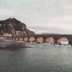 Kamienny most z wieloma łukami nad rzeką u podnóża skalistego wzgórza