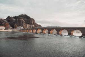 Kamienny most z wieloma łukami nad rzeką u podnóża skalistego wzgórza