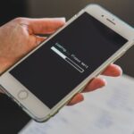 Dłoń trzymająca smartfon z wyświetlonym paskiem ładowania i napisem Loading Please Wait