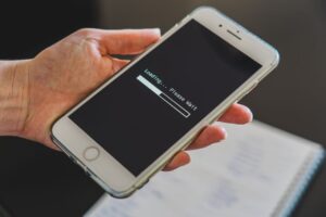 Dłoń trzymająca smartfon z wyświetlonym paskiem ładowania i napisem Loading Please Wait