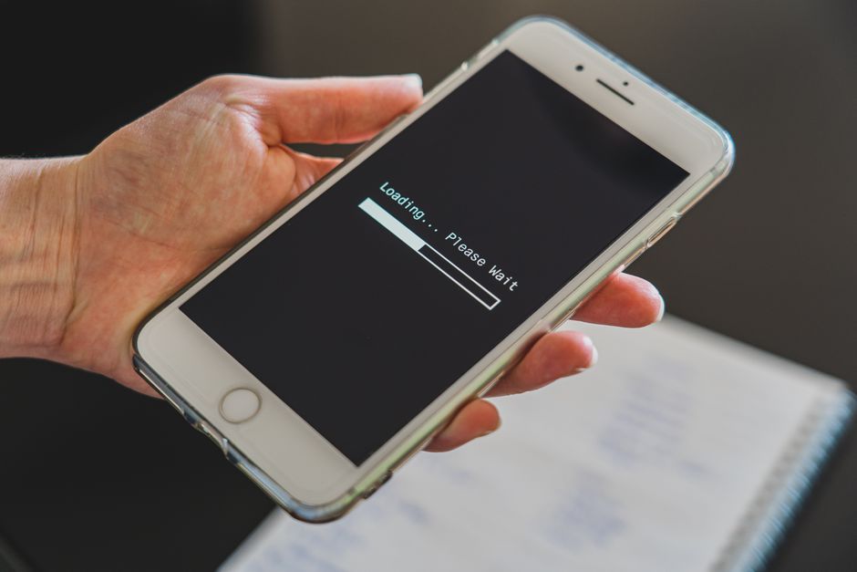 Dłoń trzymająca smartfon z wyświetlonym paskiem ładowania i napisem Loading Please Wait