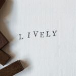 Słowo LIVELY odbite czarną czcionką na białym papierze obok drewnianych stempli.
